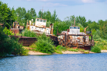 Old rusty ships lie on the riverbank. The river bank and rusting ships. Pier with old ships on the...