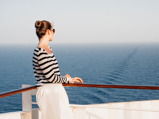 Stylish woman standing on the empty deck of a cruise ship. Sunny morning, clear day. Closeup,...