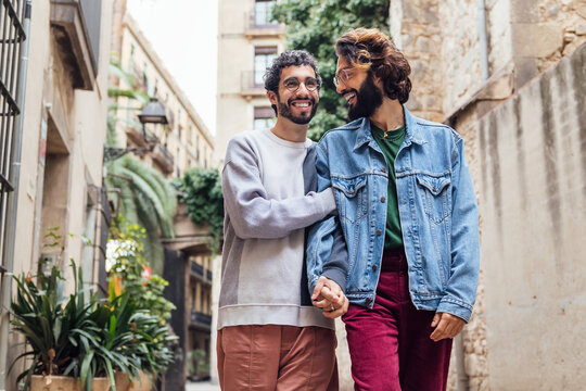 gay male couple walking embraced along a beautiful street while laughing happy, concept of lifestyle and love between people of the same sex, copy space for text
