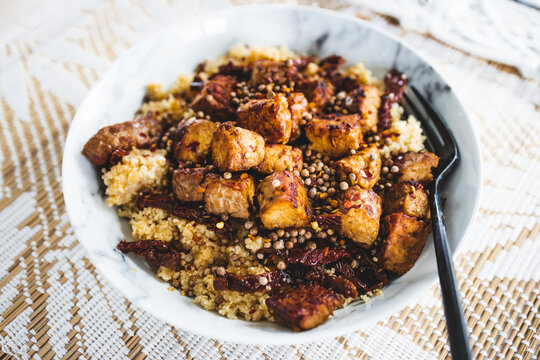 plant-based couscous with grilled tempeh cubes topped with chilli flkes and coiander seeds
