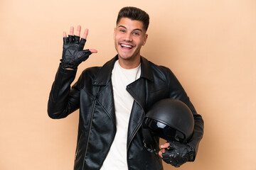 Young caucasian man with a motorcycle helmet isolated on beige background saluting with hand with happy expression