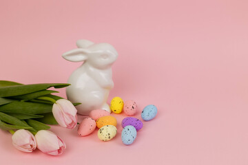 Easter card with a toy bunny, a bouquet of cyetuses and Easter eggs on a pink background, copy space