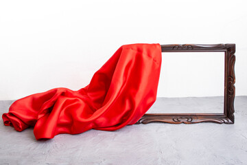 Red satin cloth unveiling a wooden brown frame, on cement table top
