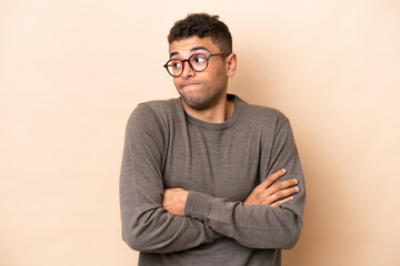 Young Brazilian man isolated on beige background making doubts gesture while lifting the shoulders