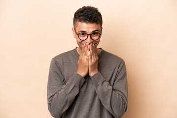Obraz premium Young Brazilian man isolated on beige background happy and smiling covering mouth with hands