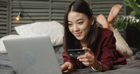 Smiling Asian woman look at laptop screen text message online on device. Happy young Japanese female use notebook browse wireless internet on gadget. Communication, technology,online shopping concept.