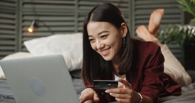 Happy Asian Young Woman Consumer Holding Credit Card And Laptop Buying Online At Home. Female Shopper Customer Shopping On Ecommerce Website Market Place Making Digital Payment Using Bonus Money.