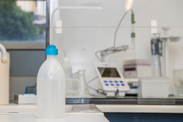 A splastic squirt bottle standing on the table in a laboratory with laboratory equiment in the background like a fume hotte and pH meter.