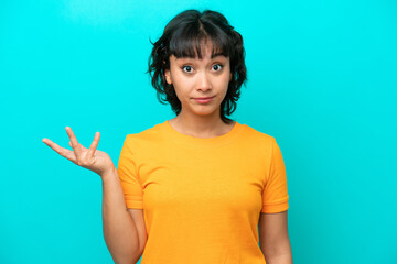 Young Argentinian woman isolated on blue background making doubts gesture