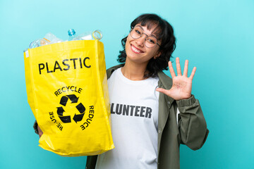 Young Argentinian woman holding a bag full of plastic bottles to recycle isolated on blue...