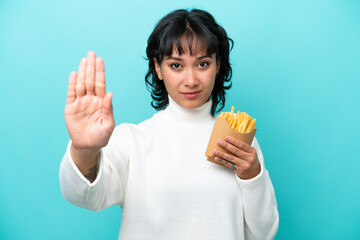 Young Argentinian woman holding fried chips isolated on blue background making stop gesture