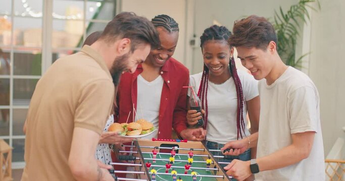 Young diverse multiethnic business creatives take break playing table football, spending day off, weekend, team, entertainment, celebrating birthday, anniversary.slow motion fun holiday for company