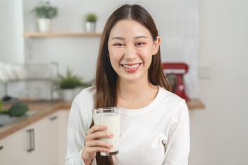 Young Asian woman holding a glass of milk in the kitchen