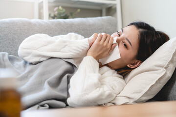 Seasonal sick concept. the young woman has a common cold and sneezing on the sofa.