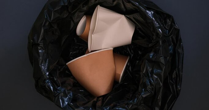 Empty paper cups fall into the trash can with a black plastic bag. Lopped 4K stop motion animation