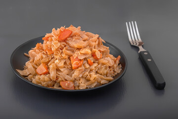 Stewed cabbage - bigos in a black plate on a dark background. Close-up