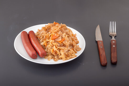 Braised cabbage - bigos and smoked sausages in a white porcelain plate. Close-up