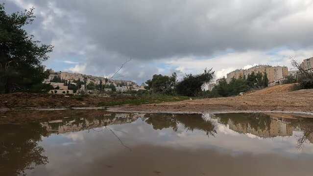 Reflection of clouds in a small puddle of water, in Deer Valley Park. Against the background of the houses of Jerusalem - Israel