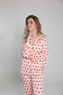 beautiful blonde girl on a white background in pajamas. pajamas with hearts. romantic pajamas. Valentine's Day. studio photo shoot in satin pajamas with a heart print. clothes for sleep and home