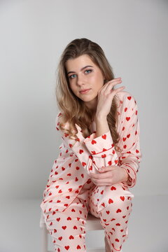 beautiful blonde girl sits on a chair on a white background in pajamas. pajamas with hearts. Valentine's Day. studio photo shoot in satin pajamas with a heart print. clothes for sleep and home