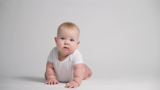 a 6-month-old baby on a white background makes an effort to get up on his hands, the first starts to uprightness