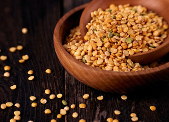 Two wooden bowls with grains of dry yellow peas on a dark wooden table