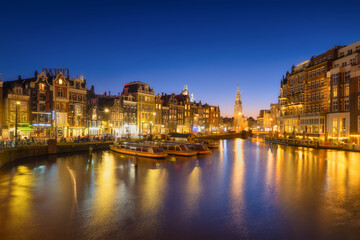 Naklejka na ściany i meble Amsterdam, Netherlands. Evening cityscape. Dark sky and city lights. Dutch canals. Reflections on the surface of the water. Photography for design and wallpaper.
