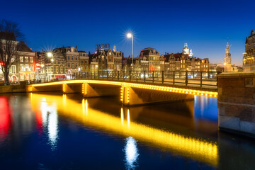 Amsterdam, Netherlands. Evening cityscape. Dark sky and city lights. Dutch canals. Reflections on the surface of the water. Photography for design and wallpaper.