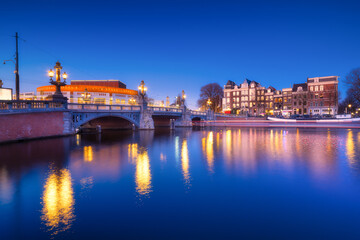 Blue bridge, Amsterdam, Netherlands. Blauwbrug. Evening cityscape. Blue sky and city lights.  Dutch canals. Reflections on the surface of the water. Photography for design and wallpaper.