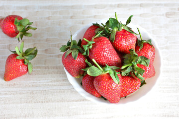 A bowl of strawberries on a table isolated on beige background, close-up