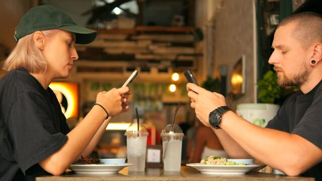 Young Mixed Race Couple Using Mobile Phones and Doesn't Talk on Dating in Restaurant, Smart Phone Social Media Addiction Problem Communication Concept 4K Footage, Thailand.