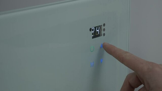 The male finger presses the touch button on the wall heater and adjusts the temperature in the room to 30. Heating system. close-up. High quality 4k footage