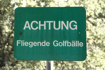 Grünes Schild mit Aufschrift: Achtung Fliegende Golfbälle