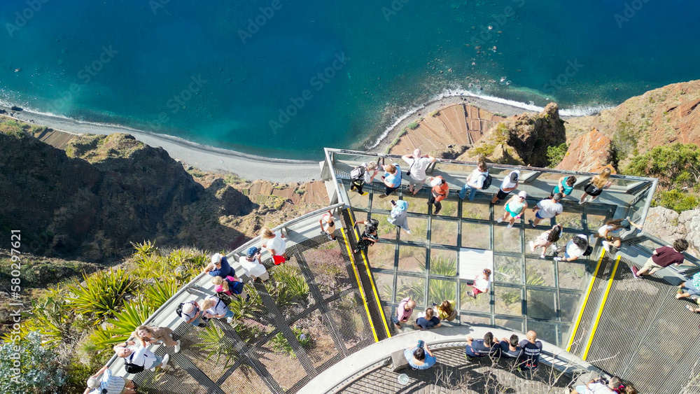 Poster tourists enjoy the viewpoint at cabo girao, along the madeira coastline, portugal. aerial view from 