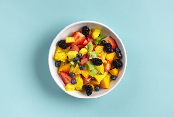 Bowl of healthy fresh summer mixed fruit salad on blue surface. Delicious and wholesome food background top view