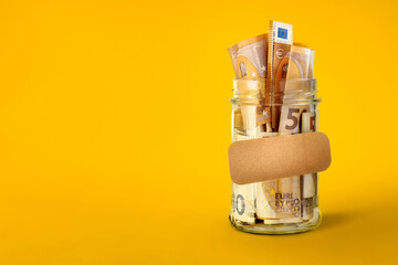 Euro bills in glass jar with blank sticker on yellow background with copy space. Saving money...