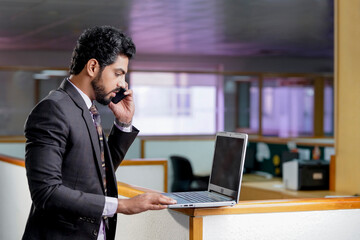 Indian businessman giving happy expression while talking on smartphone.