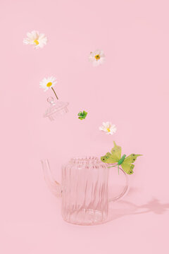 Retro Style Glass Tea Pot, Spring Flowers And Green Leaves Flying Above It, Creative Aesthetic Layout, Pastel Pink Background. Springtime Inspiration. 