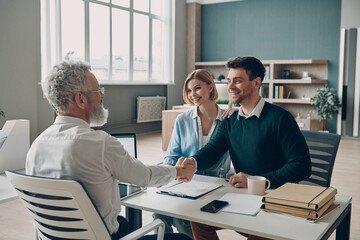 Happy young couple looking happy while man handshaking with financial advisor in the office