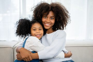 Nice girl and her mother enjoy sunny morning. Good time at home. Child giving card flower for her mom. Family playing on sofa.