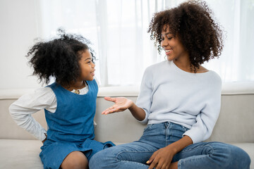 Nice girl and her mother enjoy sunny morning. Good time at home. Child giving card flower for her mom. Family playing on sofa.