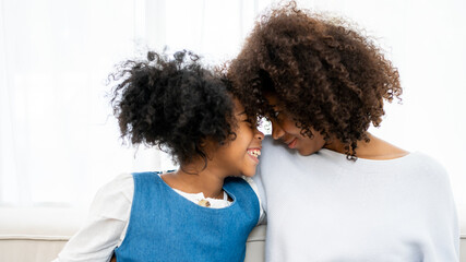 Nice girl and her mother enjoy sunny morning. Good time at home. Child giving card flower for her mom. Family playing on sofa.