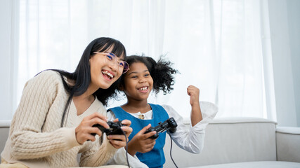African american kid , baby sitter and cute little girl having fun together, playing video games, sitting on the couch. Leisure activities, babysitting concept. - obrazy, fototapety, plakaty