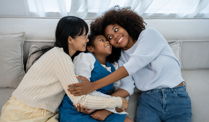 Two young women are sitting on the sofa at home in the living room and playing with their little...