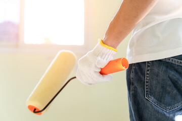 Painter man hands with gloves holds painting roller for renovation interior wall house. Worker using paint roller for decoration, painting new wall at home. Repair decoration and renovation concept.