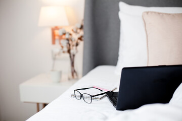 Laptop, glasses in bed. Remote working from home office. Freelance workplace in cozy bedroom. Distance learning, online education, wellbeing, healthcare