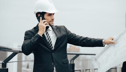 Architect manager holds blueprint standing on rooftop of skyscraper building in the city, portrait. Beard man engineer working at construction site planning building development project. Copy space.