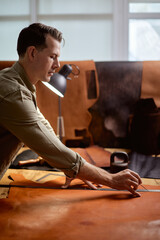 skilled tailor cuts and measures fabric according to a pattern or design at workplace. side view shot