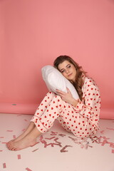 Obraz na płótnie Canvas beautiful woman in heart print pajamas on a pink background with a white pillowcase. Pink pajamas with red hearts. clothes for sleep and home. Valentine's Day. beautiful blonde in pajamas lying 