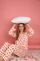 beautiful woman in heart print pajamas on a pink background with a white pillowcase. Pink pajamas with red hearts. clothes for sleep and home. Valentine's Day. beautiful blonde in pajamas lying 